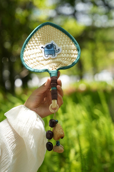 The Lucky Breeze - Hand-Woven Heart Palm Fan with Blue Elephant Charm